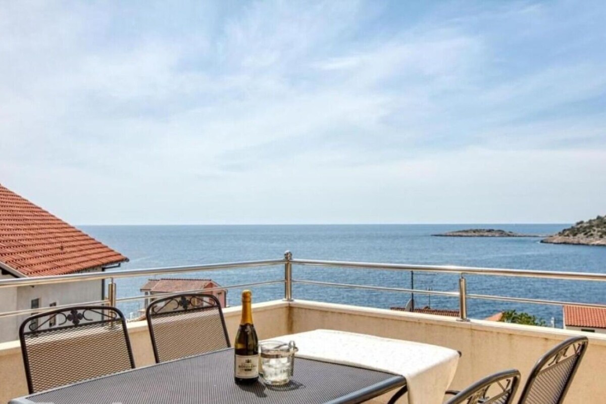 A balcony with a table, chairs, a bottle of wine, and a glass of water.