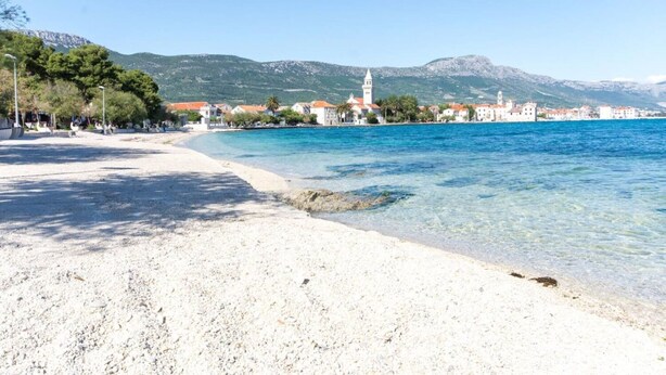 A coastal beach with clear water, a sandy shore, and buildings with red roofs in the background. - Apartment Anka (Kastela)
