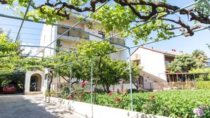 A residential building with a garden area featuring a pergola with climbing plants and flowering bushes. - Apartment Anka (Kastela)