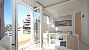 Een lichte, moderne kamer met een glazen schuifdeur naar een balkon, een klein wit bureau en een schilderij aan de muur.