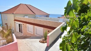 A residential building with a tiled roof, a garage, and a paved driveway. - Apartments Denko (Kali)