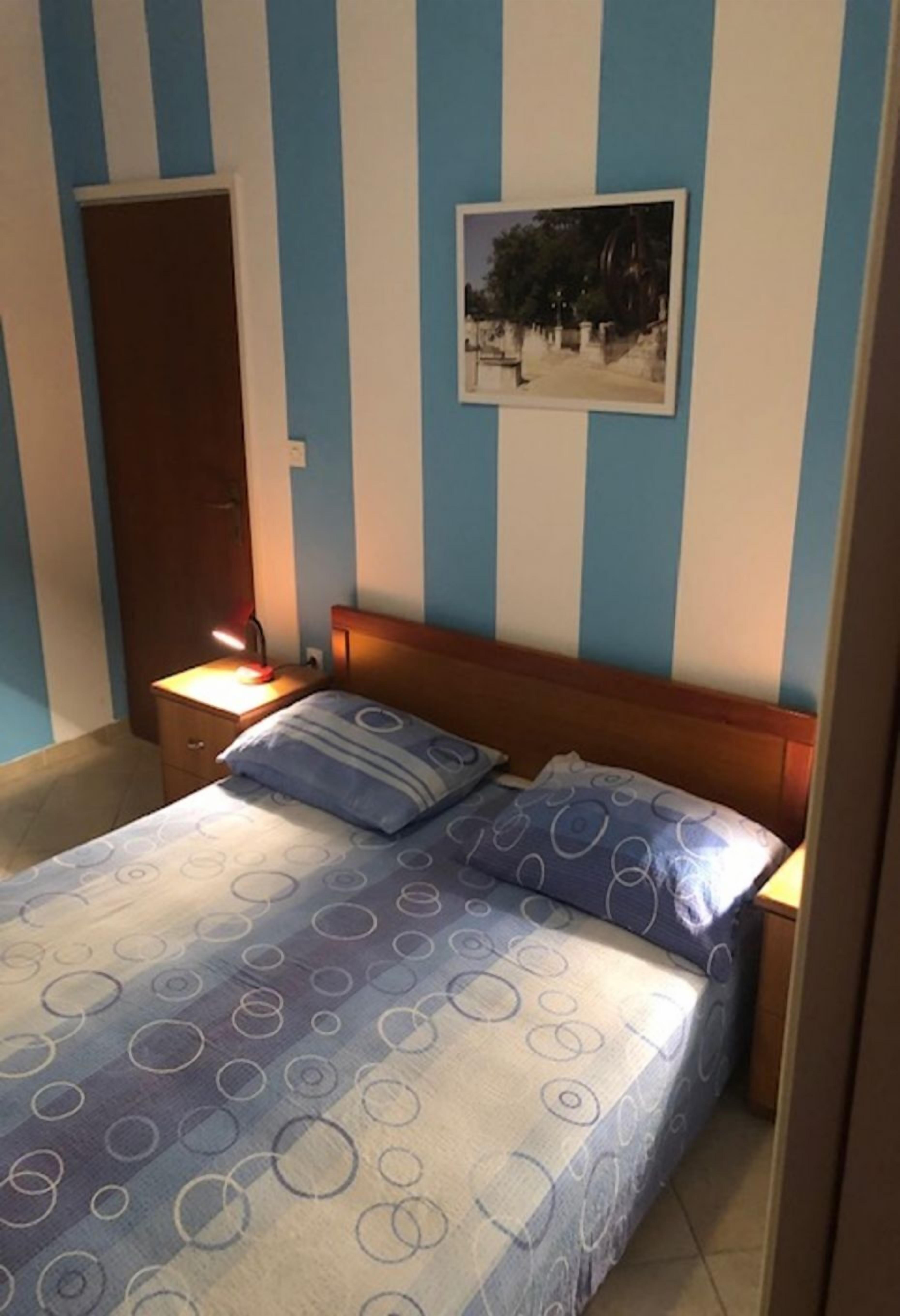 A bedroom with a bed, a nightstand, a wall-mounted picture, and a door.