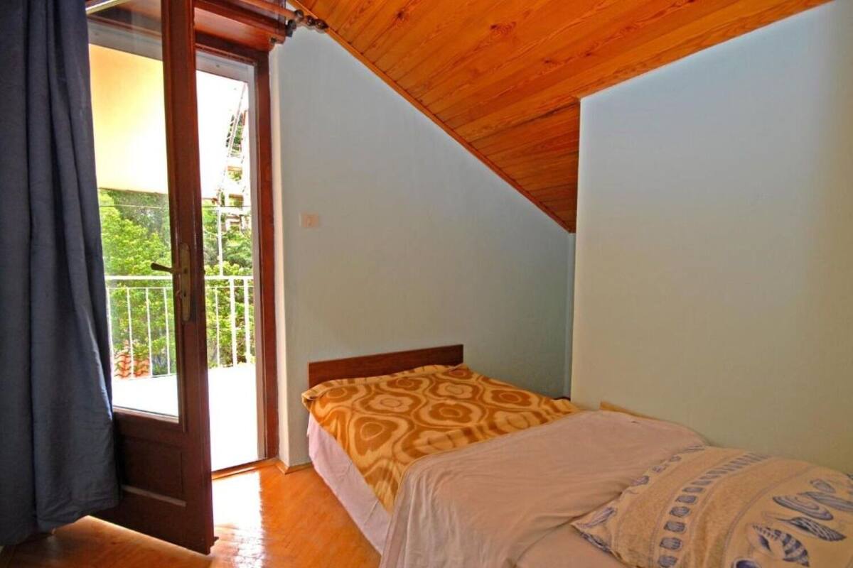 A bedroom with a bed, a wooden ceiling, and a balcony with a view of greenery.