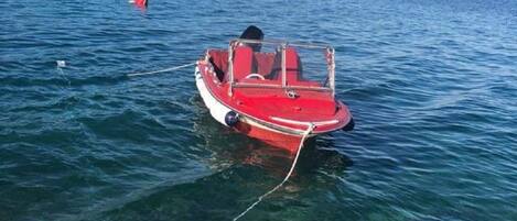 A small red boat tied to a dock with clear water and a distant shoreline.