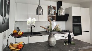 Une cuisine moderne avec des meubles blancs, un plan de travail noir, un évier, une cuisinière et des luminaires suspendus au plafond.