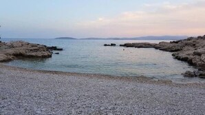 Une côte rocheuse bordée d’une eau calme et d’une terre visible au loin.