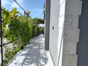 Un étroit sentier bordé d’une rambarde métallique d’un côté et d’un mur recouvert de grandes carreaux de couleur claire de l’autre.