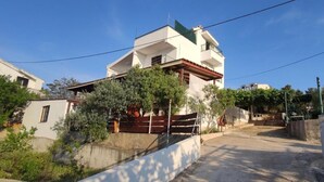 A two-story residential building with a balcony, surrounded by greenery and a concrete wall. - Apartments Vlado (Solta)
