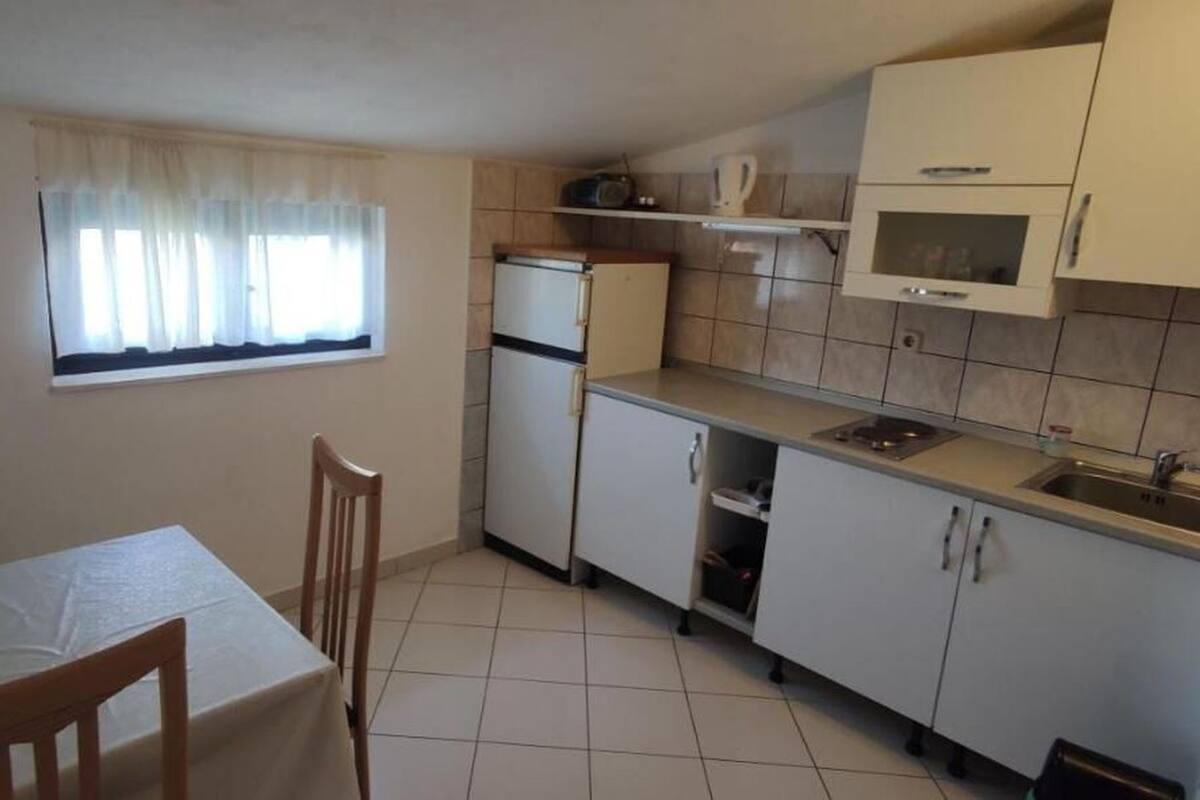 A compact kitchen with a dining table and chairs, a refrigerator, a microwave, and a window with curtains.