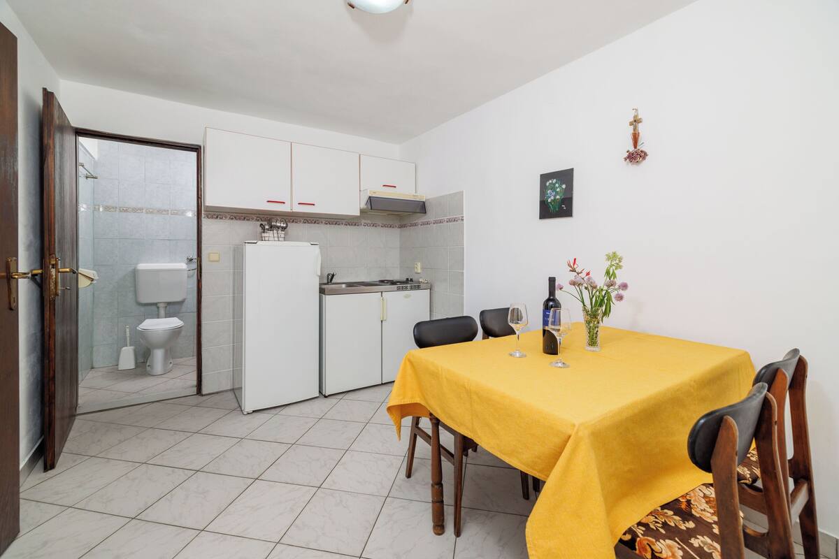 Une cuisine compacte avec des meubles blancs, une table à manger recouverte d’une nappe jaune et un petit coin repas.