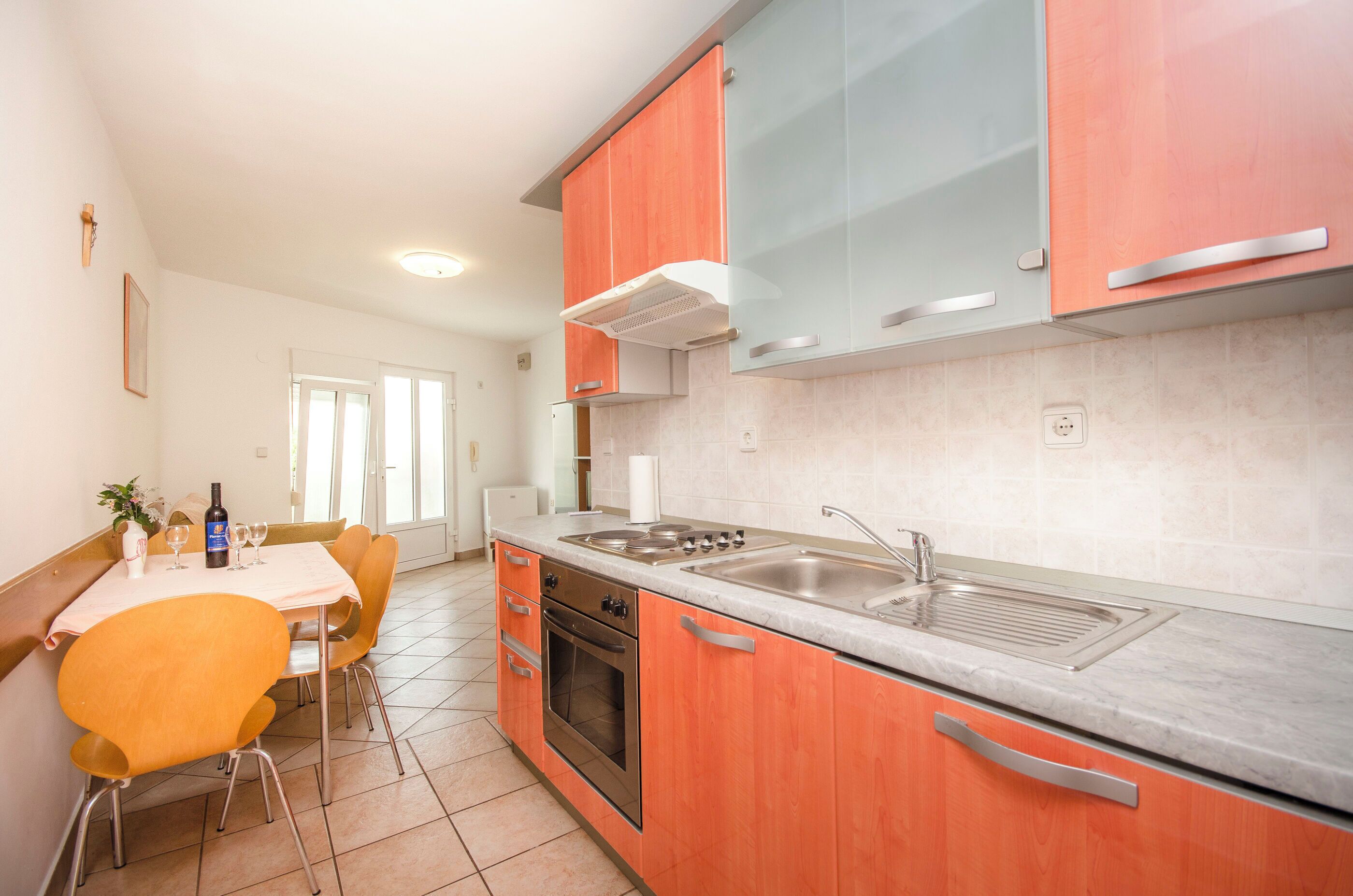 A modern kitchen with orange cabinets, a stainless steel sink, and a dining area with a table and chairs.