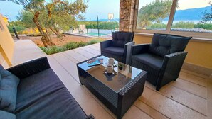 An outdoor seating area with wicker furniture and a glass table, overlooking a pool and landscape. - House Fani (Postira)
