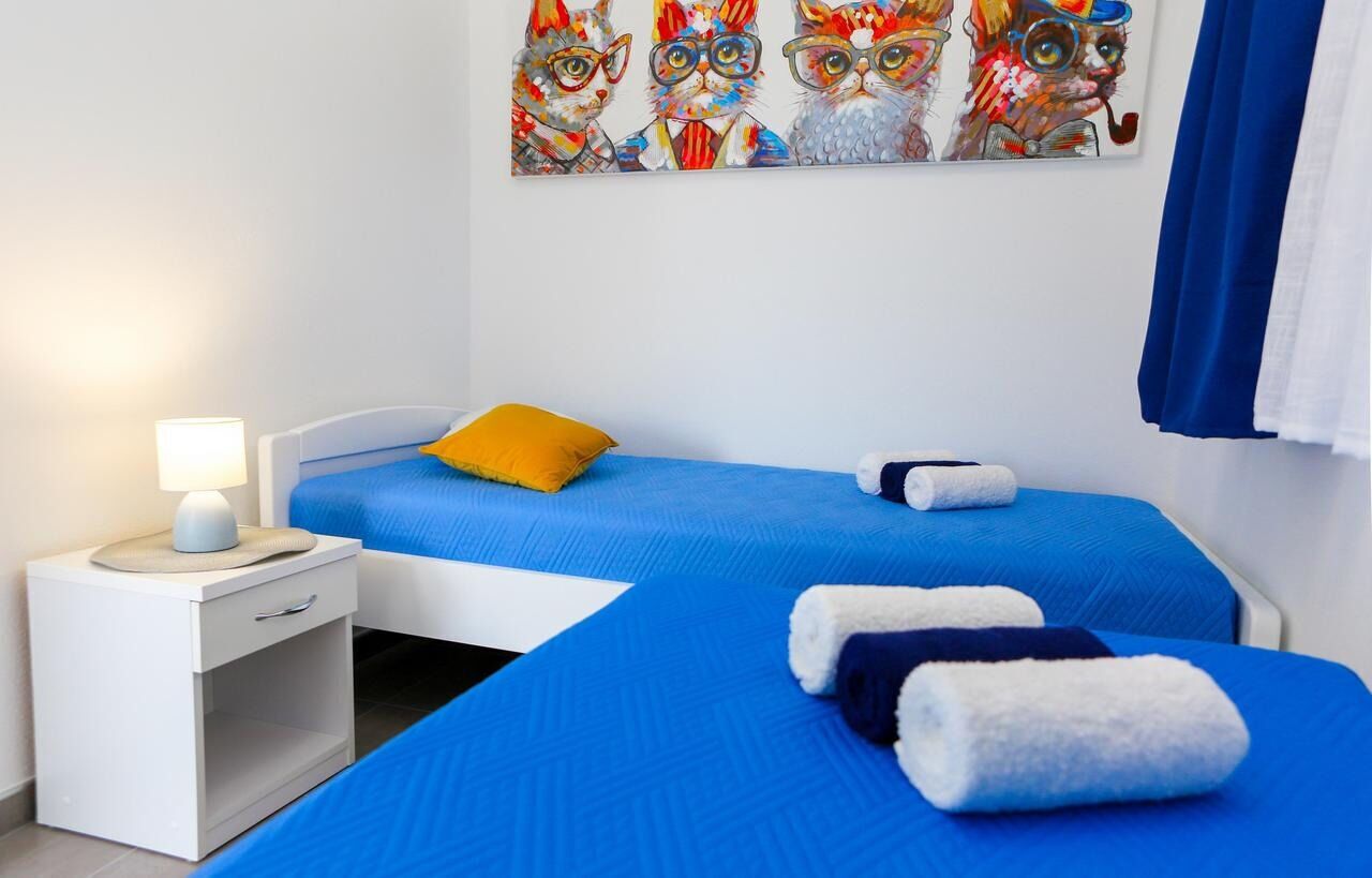Una habitación de hotel con dos camas, una mesita de noche, una lámpara y un cuadro de lechuzas en la pared.