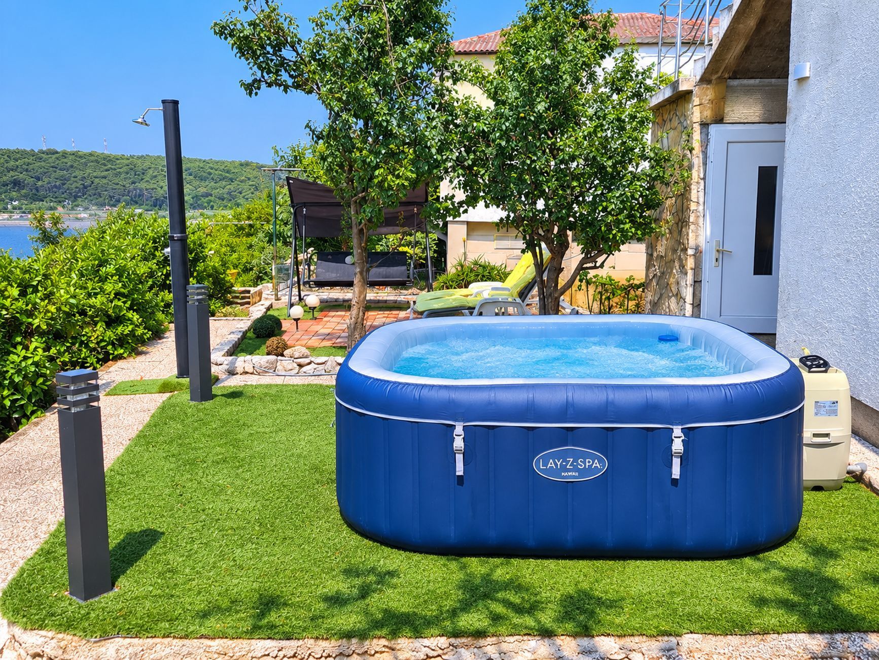 A backyard with a blue inflatable hot tub, a patio with outdoor furniture, and a view of a body of water.