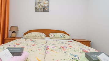 Ein Doppelbett mit floralem Bettbezug, eine Nachttischlampe, ein Bild an der Wand und eine 'Welcome'-Box auf dem Nachttisch.