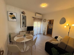 A living room with a round dining table, a sofa, a TV, a kitchen area, and a ceiling light. - Apartments Ivi (Rab)