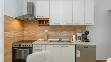 A compact kitchen with a stove, oven, sink, and coffee maker.