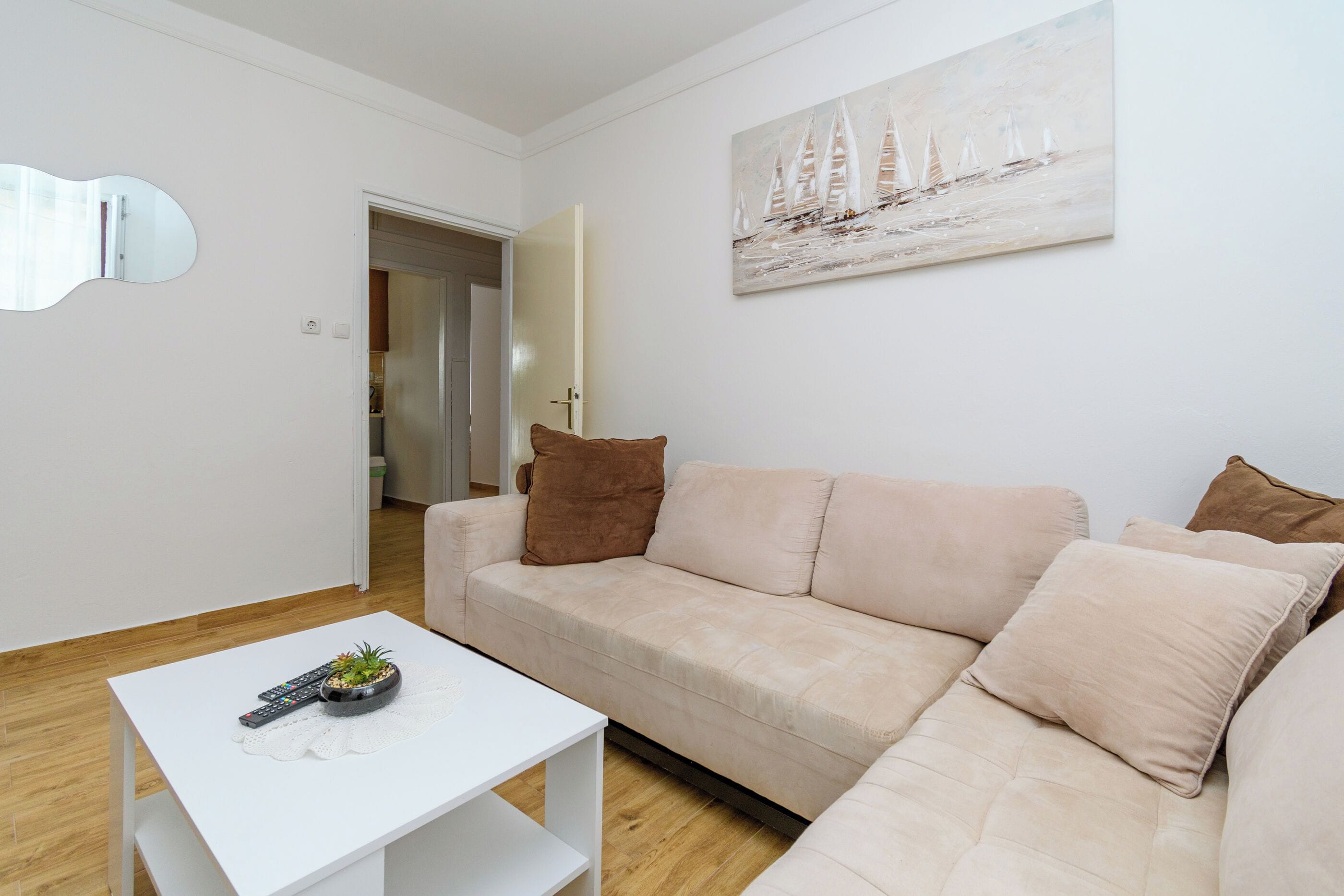 A modern living room with a beige sofa, a white coffee table, and a painting of sailboats.