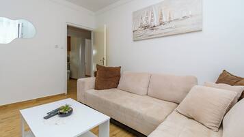 A modern living room with a beige sofa, a white coffee table, and a painting of sailboats.