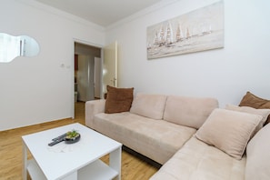 A modern living room with a beige sofa, a white coffee table, and a painting of sailboats. - Apartments Ivi (Rab)