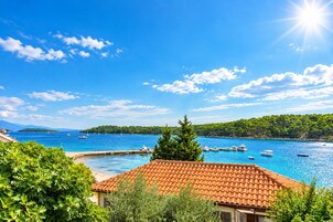 Vista costeira com céu claro, corpo de água, barcos e um edifício com telhado de azulejos.