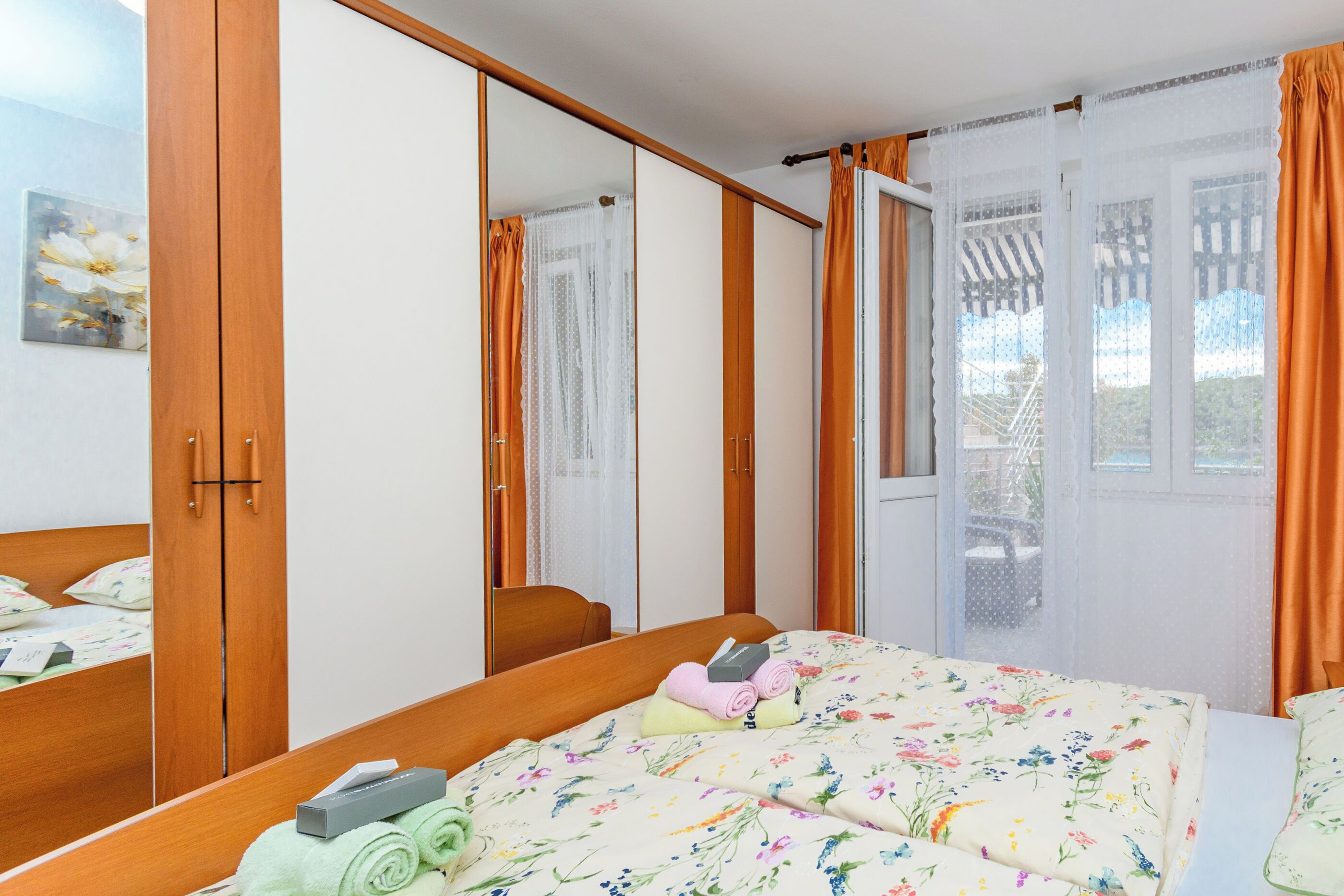Quarto com cama, guarda-roupa, espelho e janela com cortinas.