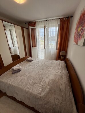 Un dormitorio con cama, mesita de noche, lámpara, espejo y ventana con cortinas.
