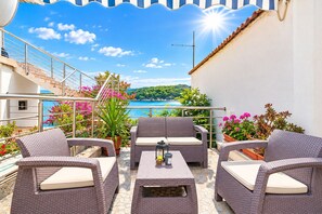 A balcony with wicker furniture, potted plants, and a view of the sea. - Apartments Ivi (Rab)