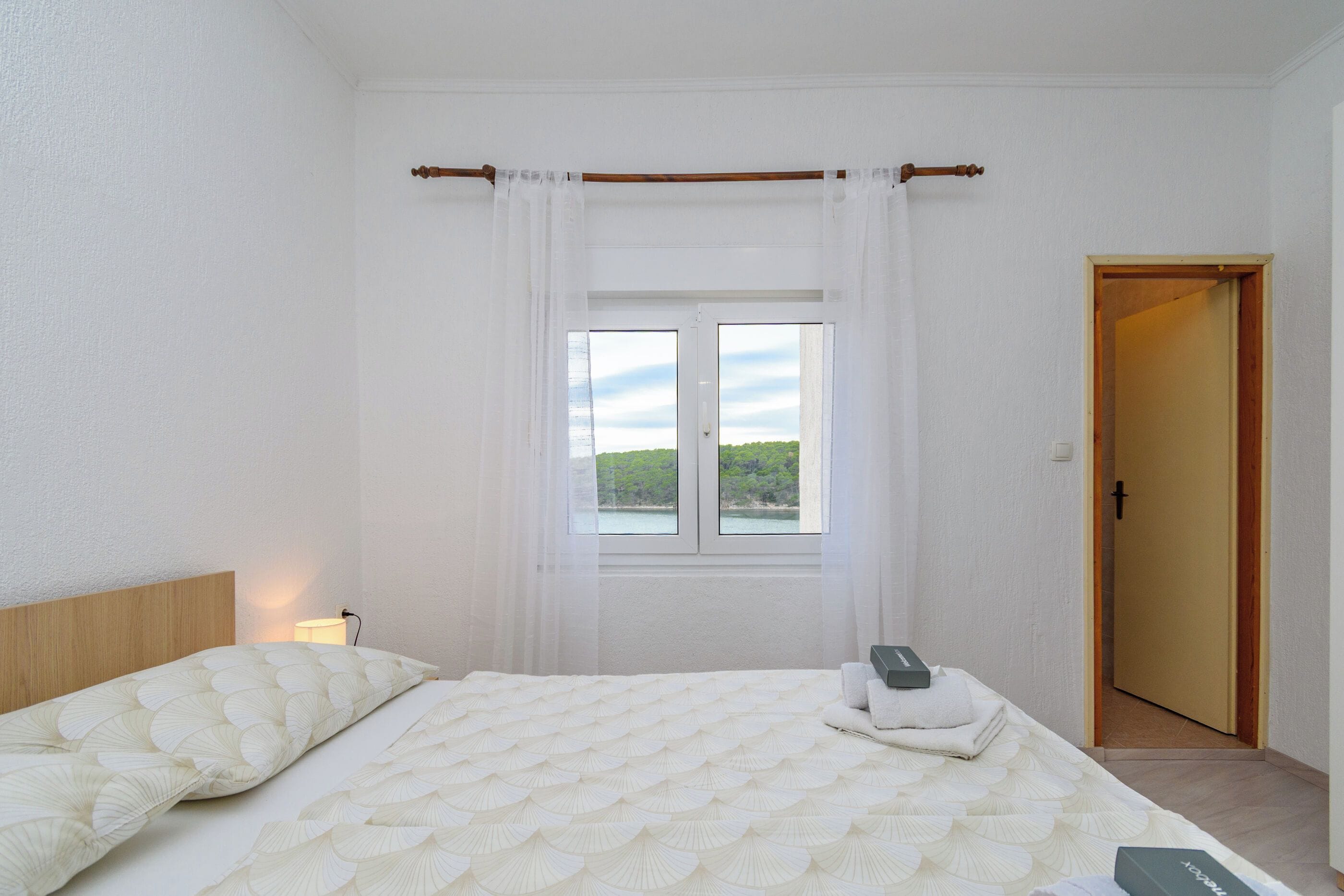 Une chambre à coucher avec un lit, une fenêtre avec des rideaux, une lampe de chevet et une porte.