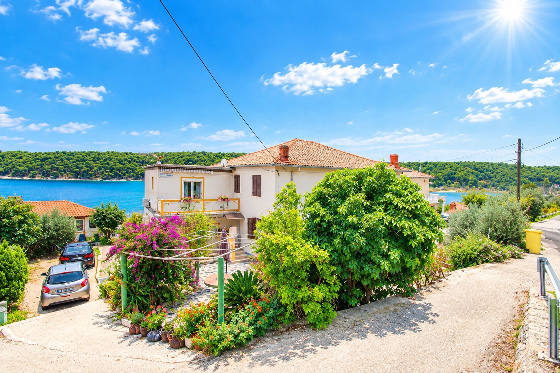 A coastal house with a tiled roof, surrounded by lush greenery and a clear view of the sea.