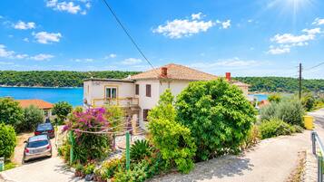 A coastal house with a tiled roof, surrounded by lush greenery and a clear view of the sea.