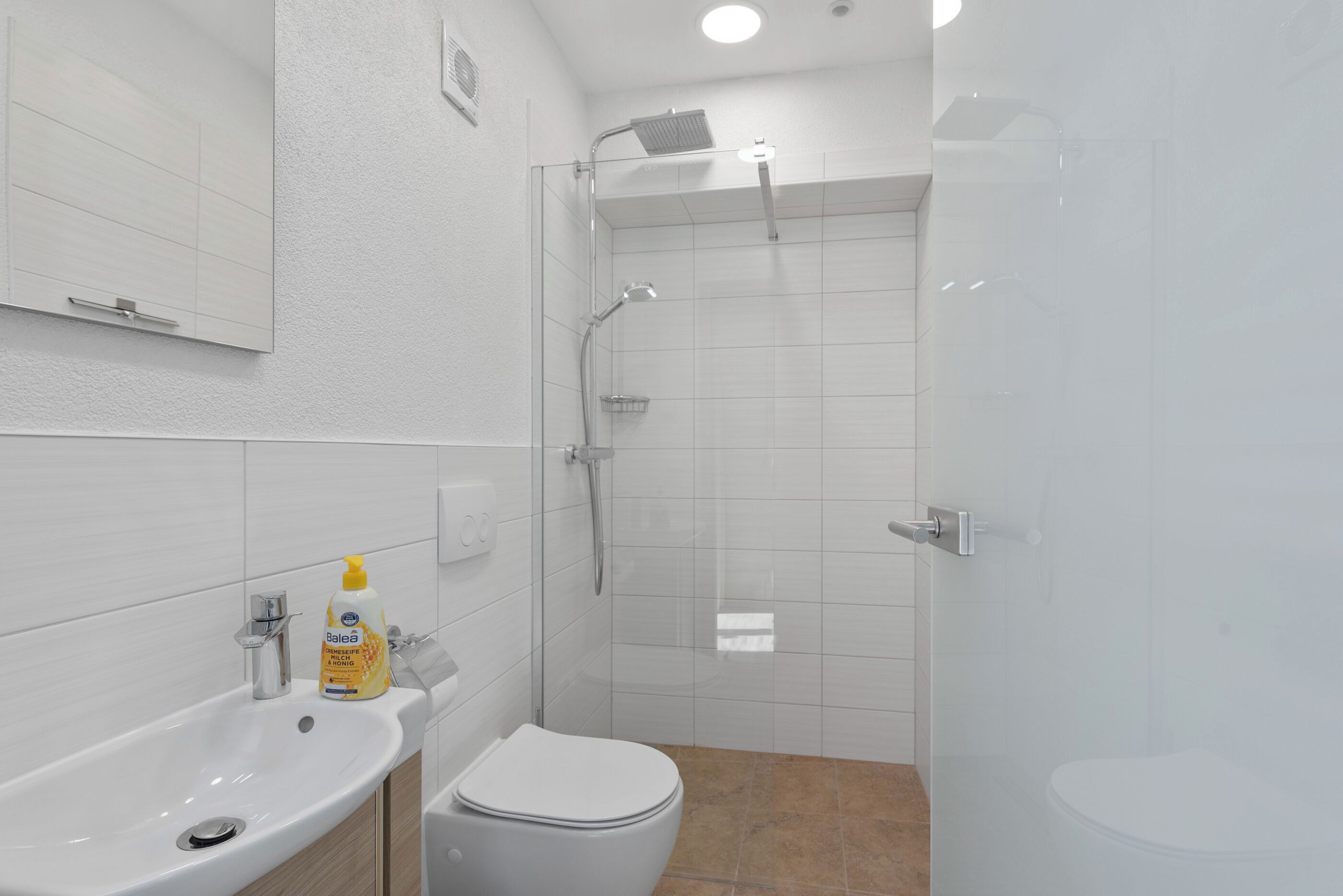 A modern bathroom with a white sink, a toilet, and a glass-enclosed shower area.