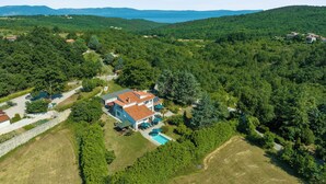 Vista aerea di una proprietà con una grande casa, una piscina e dolci colline boschive tutt'intorno.