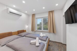 Une chambre d’hôtel avec deux lits, un appareil de climatisation, une fenêtre avec des rideaux et un téléviseur à écran plat.