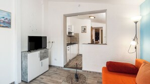 Ein modernes Wohnzimmer mit einem Glastisch, einem Flachbildfernseher und einem orangefarbenen Sofa.