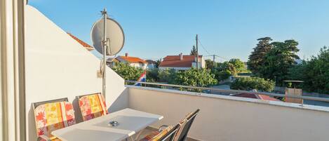 Un balcón con mesa y sillas, una antena parabólica y vistas a casas y árboles.