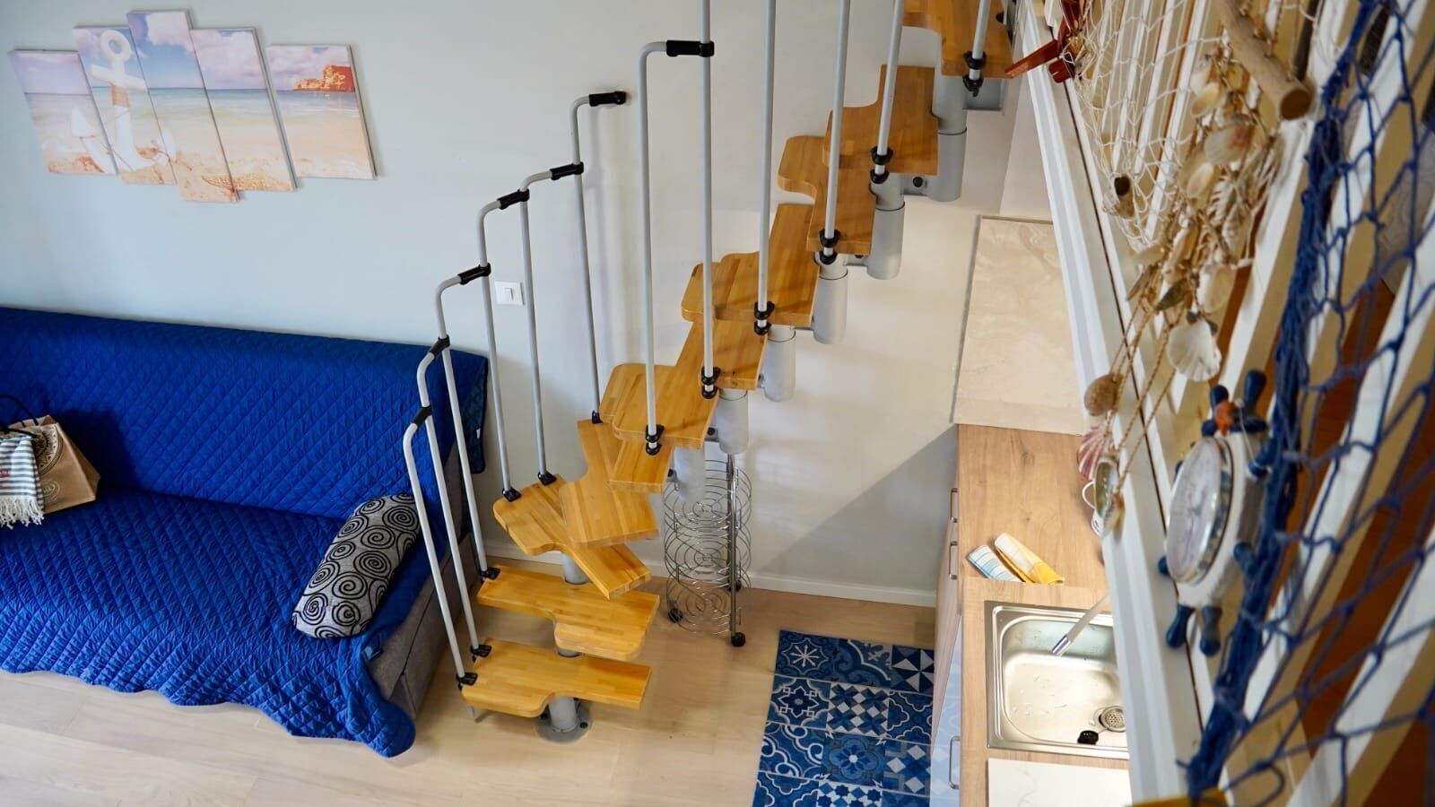 Una habitación con un sofá azul, una escalera de madera y un perro pequeño.