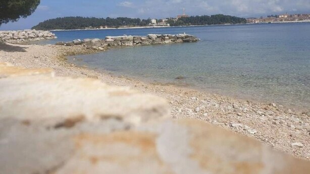 Paisaje costero con costa rocosa, agua cristalina y una isla distante con edificios.