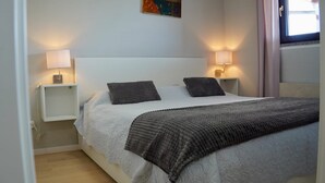 Un dormitorio con una cama, dos lámparas de noche, una mesita de noche y una ventana con cortinas.