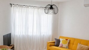 Ein modernes Wohnzimmer mit einem gelben Sofa, einem Glastisch und einem Rattaneschekel.