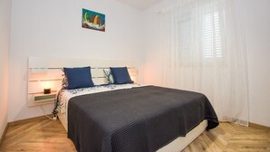 Ein Schlafzimmer mit Bett, Nachttisch, Nachttischlampe, einem Bild an der Wand und einem Fenster mit Vorhängen.