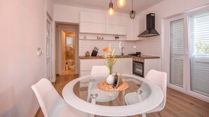 A modern kitchen with white cabinets, a round glass table, and a vase of flowers. - Apartments Ned (Kolan)