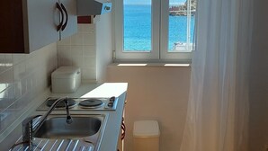 Eine Küche mit Meerblick, ein Fenster mit weißen Vorhängen und ein Fischgrätparkettboden.