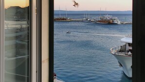 Blick aus einem Fenster auf einen Jachthafen mit mehreren vertäuten Booten, einem klaren Himmel und einem fliegenden Vogel.