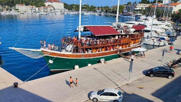 Ein großes Boot liegt in einer Marina vor Anker, mit einer Fußgängerbrücke und einem Auto im Vordergrund.