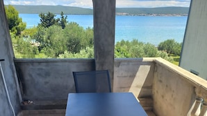 Un balcon avec une table et des chaises, donnant sur une étendue d’eau et sur de la verdure.
