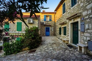 A narrow cobblestone street flanked by stone buildings with green shutters and a central blue door. - Apartment Vinci 1906 (Vrsar)
