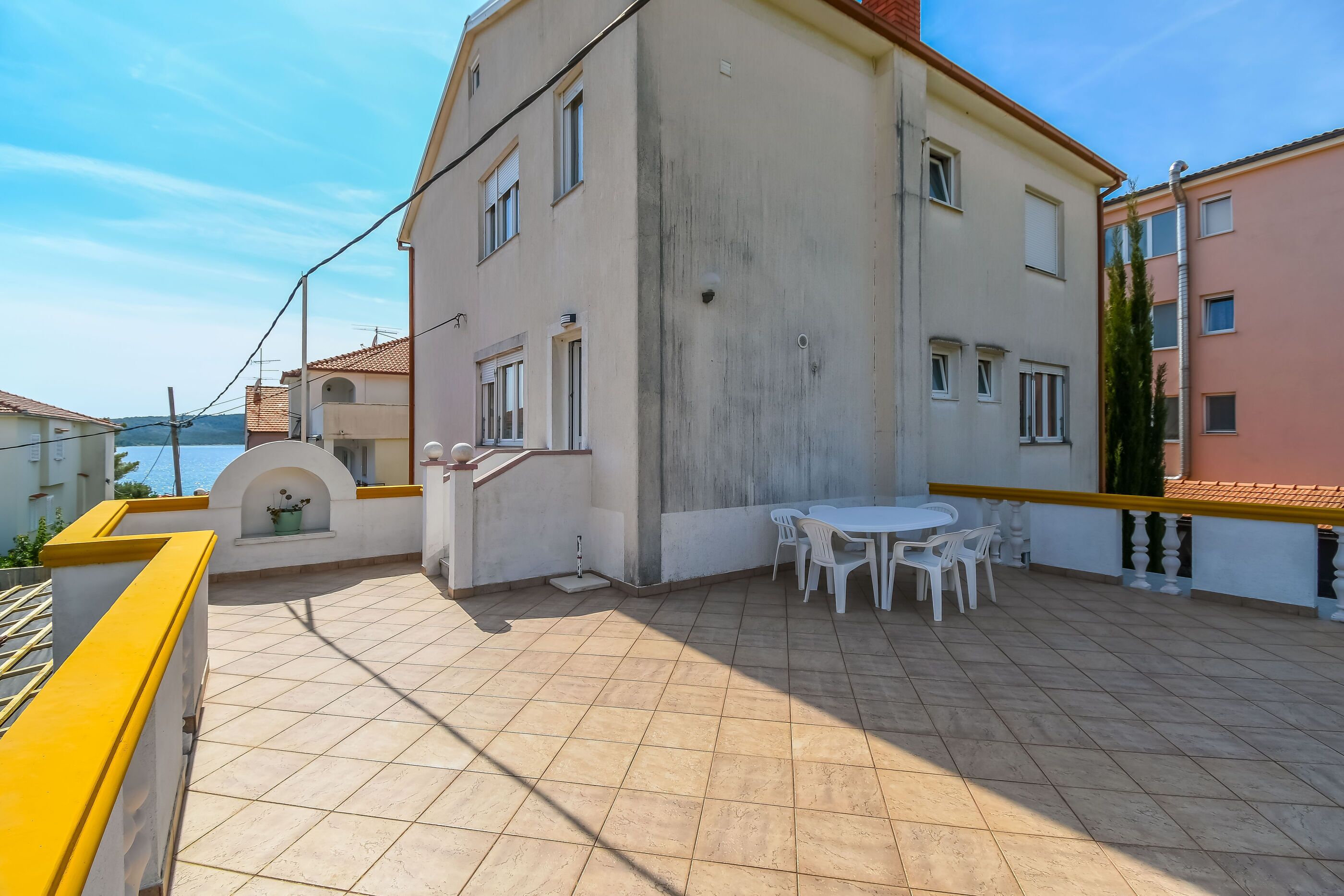 Un edificio residencial con un patio empedrado, una pequeña mesa con sillas y una barandilla amarilla.