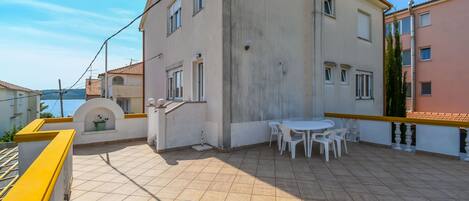 Un edificio residencial con un patio empedrado, una pequeña mesa con sillas y una barandilla amarilla.