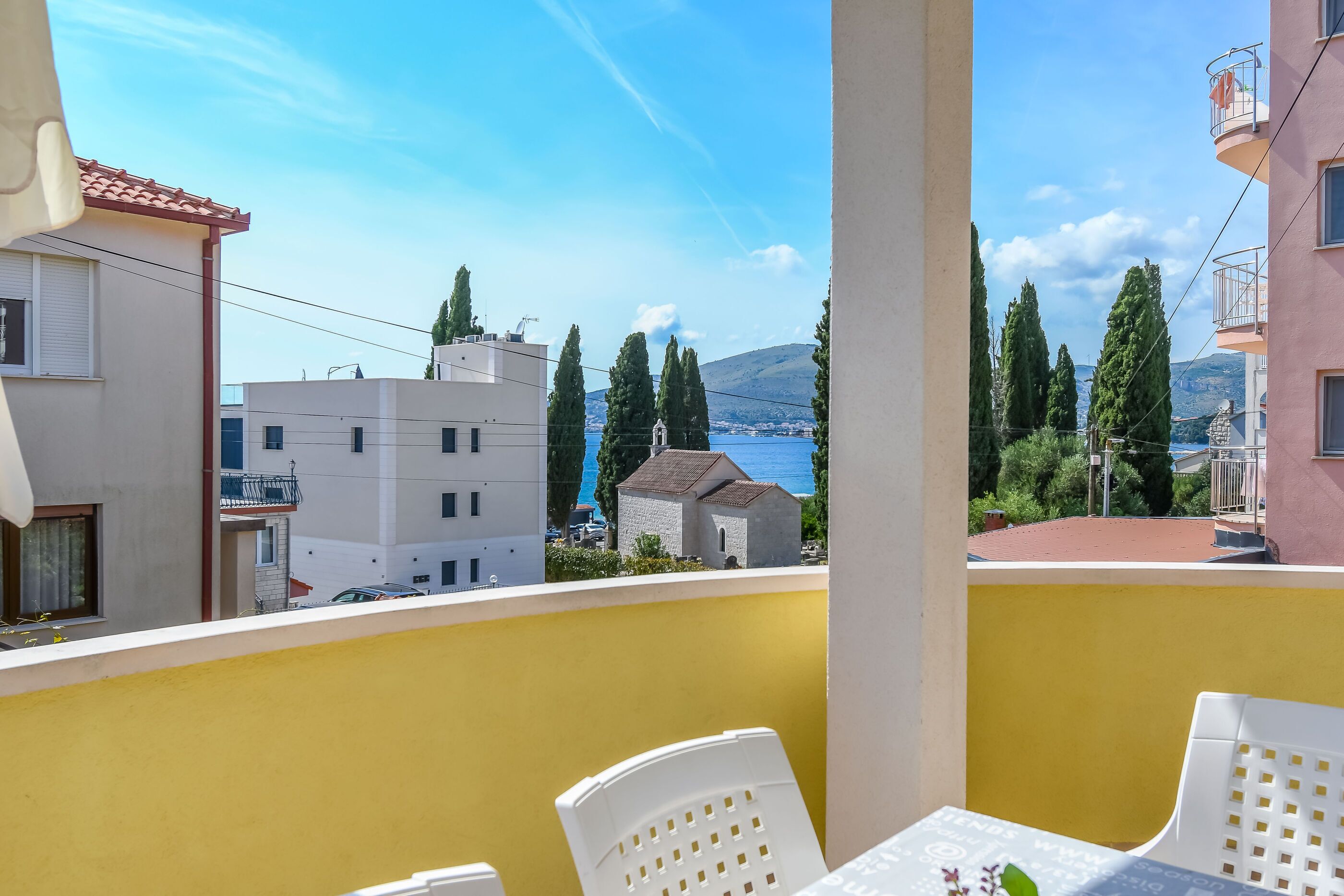 A balcony with yellow walls, white chairs, and a table.